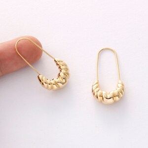 May include: A pair of gold hoop earrings with a twisted design. The earrings are made of metal and have a simple, elegant style.
