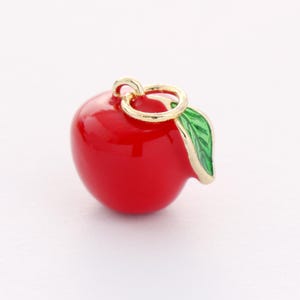 May include: A red apple charm with a gold ring and a green leaf. The charm is perfect for adding a touch of whimsy to jewelry or crafts.