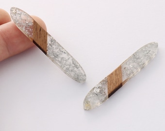 Puede incluir: Dos pendientes de resina transparente y madera con purpurina plateada incrustada en la resina. Los pendientes tienen forma de óvalos largos con una raya de madera diagonal.