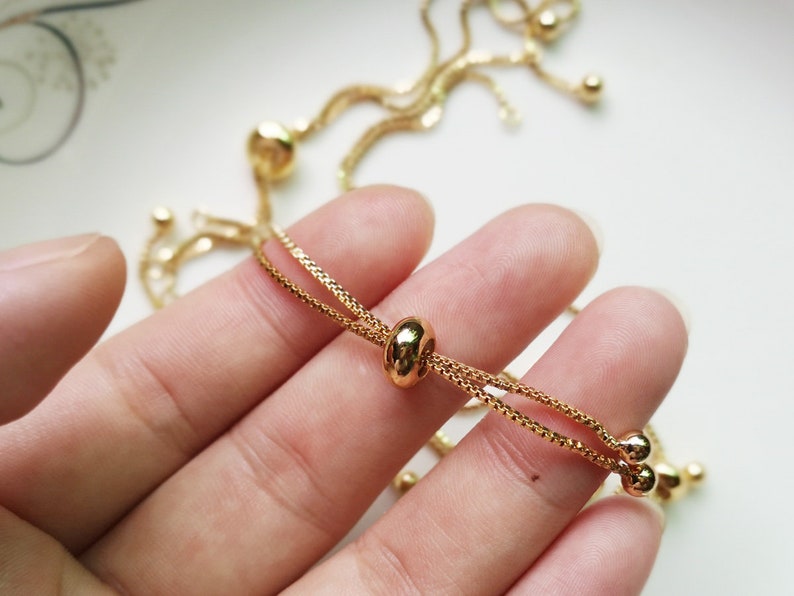 May include: A gold chain bracelet with a sliding clasp. The bracelet is made of two thin chains that are connected by a small gold bead.
