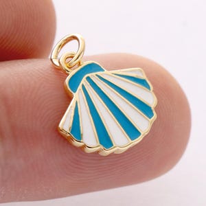 Può includere: Un ciondolo a forma di conchiglia color oro con un design smaltato blu e bianco. Il ciondolo ha un piccolo anello per attaccarlo a una collana o un braccialetto. Il design della conchiglia è dettagliato e accattivante.