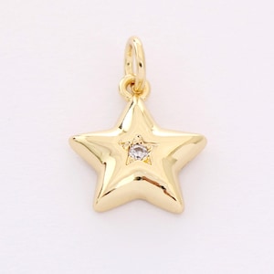 May include: A gold star charm with a small clear rhinestone in the center. The charm has a loop at the top for attaching to a necklace or bracelet.