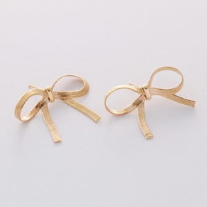 May include: A pair of gold bow-shaped earrings. The earrings are made of a thin, textured metal and have a simple, elegant design.