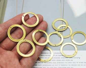 May include: A hand holding a group of eight brass rings with a hole in each ring. The rings are all the same size and have a smooth, polished finish.