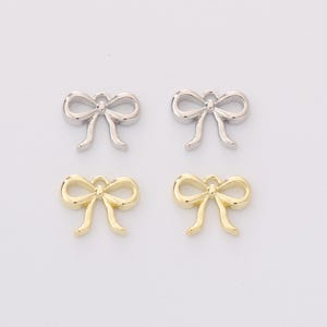 Op de afbeelding: Vier strikvormige bedels. Twee zijn zilverkleurig en twee goudkleurig. Elke bedel heeft een lus aan de bovenkant om aan sieraden of andere knutselwerken te bevestigen. De strikken hebben een klassiek, elegant ontwerp.