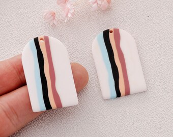 Könnte beinhalten: Zwei weiße Polymer Clay Ohrringe in abgerundeter rechteckiger Form. Die Ohrringe haben ein Muster aus schwarzen, hellblauen, rosa und orangefarbenen Streifen.
