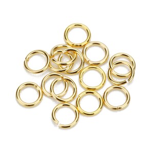 May include: A pile of 12 gold jump rings, a type of jewelry finding used for connecting chains, cords, and other jewelry components.