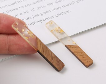 Puede incluir: Dos pendientes rectangulares de resina y madera con detalles de pan de oro. La resina es transparente y la madera es marrón.