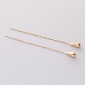 May include: A pair of gold dangle earrings with a teardrop shape at the end of each chain.