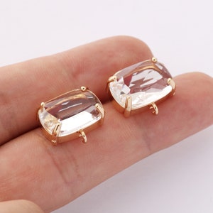 Puede incluir: Dos colgantes rectangulares de cristal transparente con engastes de metal dorado. Cada colgante tiene un lazo en la parte inferior para sujetarlo a una joya. Los cristales están facetados, captando la luz.