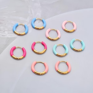 May include: A selection of hoop earrings in various colours. The earrings have a gold-tone metal base with a bright enamel coating in shades of blue, pink, and turquoise. The earrings are small and circular, suitable for everyday wear.