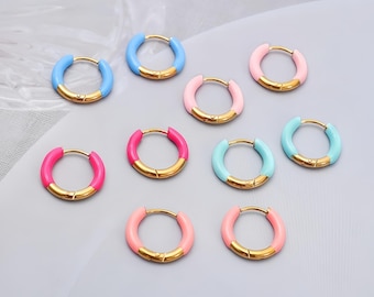 Puede incluir: Una colección de pendientes de aro coloridos. Los pendientes presentan una base de metal dorado con un vibrante revestimiento de esmalte en tonos de azul, rosa y turquesa. Los pendientes son pequeños y circulares, adecuados para el uso diario.
