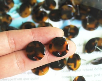 May include: Two brown and black tortoise shell round buttons with a hole in the center. The buttons are on a finger.