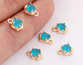 Puede incluir: Seis dijes dorados con un centro de piedra preciosa azul claro y redondo. Cada dije tiene un pequeño lazo y un engaste decorativo alrededor de la piedra preciosa. Los dijes son pequeños, probablemente para la fabricación de joyas.