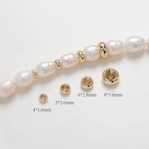 Pode incluir: Quatro anéis de salto de metal dourado de diferentes tamanhos. Os anéis são mostrados ao lado de um fio de pérolas brancas. Os tamanhos são etiquetados como 4*1,6 mm, 5*2,6 mm, 6*2,8 mm e 8*3,8 mm.