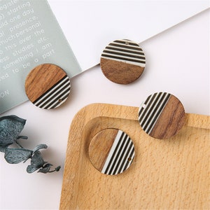 May include: Four round wooden and white striped pendant charms with a hole for stringing. The charms are on a wooden surface.