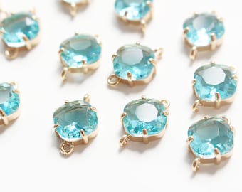 Op de afbeelding: Tien turquoise blauwe glazen connector charms met gouden metalen accenten. De charms zijn vierkant met afgeronde hoeken en hebben aan elke kant een gat om aan sieraden te bevestigen.