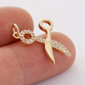 May include: Gold-tone scissors charm with clear cubic zirconia stones. The charm has a loop for attaching to a necklace or bracelet.