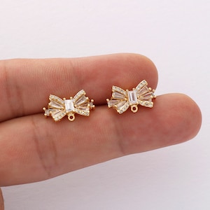 May include: Two gold-tone bow-shaped charms with clear cubic zirconia stones. Each charm has a jump ring for attaching to jewelry.