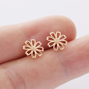 Puede incluir: Un par de pendientes de botón de oro en forma de flor. Los pendientes son delicados y tienen un diseño sencillo.