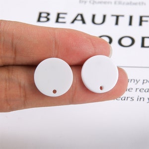 May include: Two white round acrylic blanks with a small hole in the center. The blanks are approximately 1 inch in diameter.