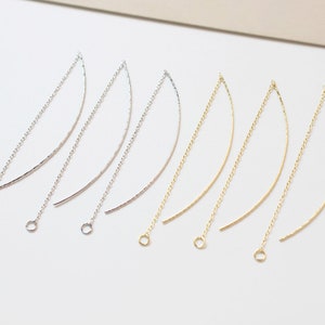 May include: Six gold and silver earring hoops with a curved shape. The hoops are made of thin metal and have a delicate, minimalist design.