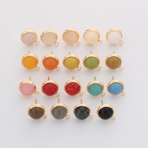 Pode incluir: Uma coleção de dezanove componentes de brincos redondos dispostos em quatro filas. Cada peça apresenta um cabochão circular liso em várias cores sólidas e padrões de pedra, montado numa armação de metal dourado com um pequeno aro.