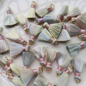 Puede incluir: Una colección de borlas multicolores y coloridas con anillos dorados. Las borlas están hechas de un material suave y sedoso y tienen un ribete rosa.