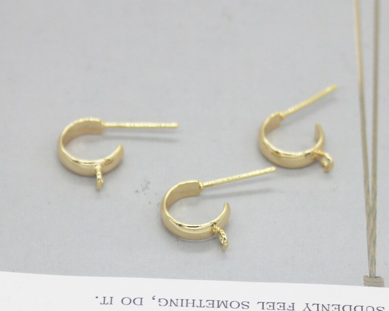 May include: Three gold-toned earring hoops with a small loop at the bottom and a straight pin attached to the top.