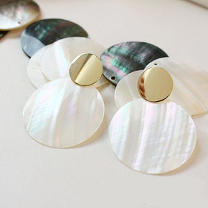 May include: A pair of earrings with a layered design featuring iridescent white and black shell-like discs with gold accents.