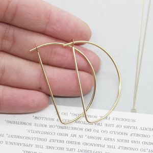 May include: A pair of gold hoop earrings with a geometric design. The earrings are made of thin metal and have a simple, modern look.