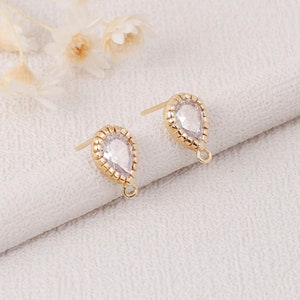May include: A pair of gold-tone teardrop-shaped earring findings with clear crystal accents. The findings have a loop at the bottom for attaching a dangle charm.