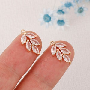 May include: A pair of gold-tone earring charms featuring a delicate leaf design with clear cubic zirconia stones.