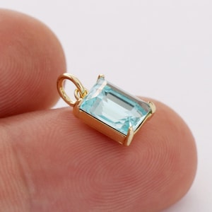 May include: Gold pendant with a light blue emerald-cut gemstone.
