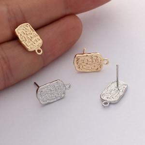 May include: Two pairs of earring findings with textured rectangular charms. One pair is gold and the other is silver.