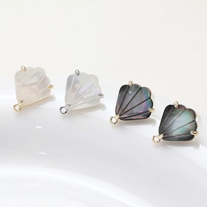 May include: Four shell-shaped earring charms with gold jump rings. Two charms are white and two are black with iridescent accents.