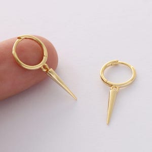 May include: A pair of gold hoop earrings with a small, pointed spike dangling from each hoop.