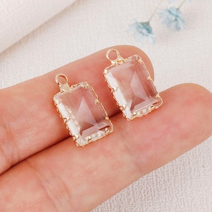 May include: Two gold-tone pendant charms with clear glass rectangular stones. The stones are set in a gold-tone frame with a decorative edge.