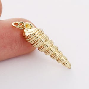 Puede incluir: Encanto de concha de mar de tono dorado con un diseño en espiral. El encanto tiene un bucle en la parte superior para sujetarlo a un collar o pulsera.