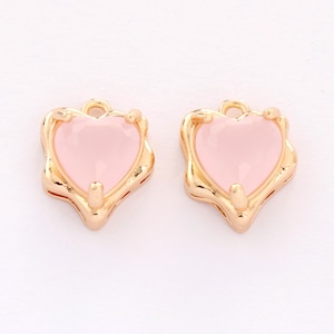 Puede incluir: Dos colgantes en forma de corazón de tono dorado con inserciones de vidrio rosa. Los colgantes tienen un borde festoneado decorativo.