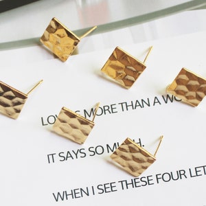 May include: Five gold-toned metal earring studs with a hammered texture. The studs are arranged on a white surface with text.