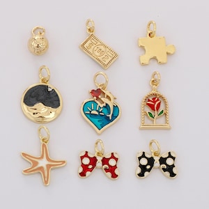 May include: A collection of gold-colored charms with various designs, including a soccer ball, a puzzle piece, a dollar bill, a black and gray design, a heart with dolphins, a rose in a cage, a starfish, and two bowties with polka dots.
