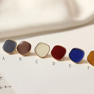 Op de afbeelding: Zes kleine, vierkante emaillepins met gouden metalen frames. De pins zijn in de kleuren blauw, bruin, wit, rood, donkerblauw en geel.