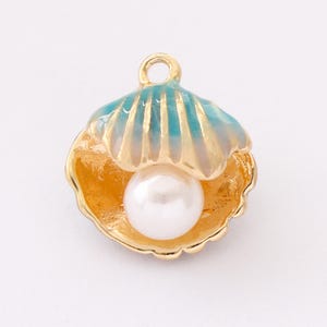 May include: A gold-coloured seashell charm with a pearl inside. The shell has a light blue and gold top, and a gold-coloured base. The pearl is white and round. The charm has a small loop at the top for attaching to a necklace or bracelet.