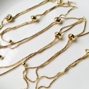 May include: A set of gold-toned adjustable bracelets with small round beads and a larger oval bead on each bracelet.
