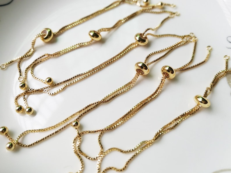 May include: A set of gold-toned adjustable bracelets with small round beads and a larger oval bead on each bracelet.