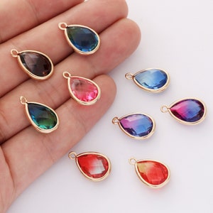 May include: Assortment of eight teardrop-shaped glass charms with gold-tone metal settings. The charms are in various colors, including blue, green, red, and pink.