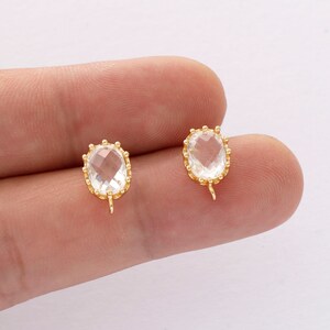 May include: Two gold-tone earring findings with clear oval-shaped glass stones set in a beaded bezel.