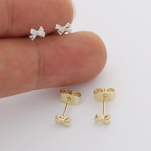 Peut inclure: Deux paires de petites boucles d'oreilles à tige en forme de nœud. Une paire est de couleur argentée et l'autre est de couleur dorée. Chaque boucle d'oreilles est dotée d'une tige et d'un fermoir papillon en métal assorti pour la fixation.
