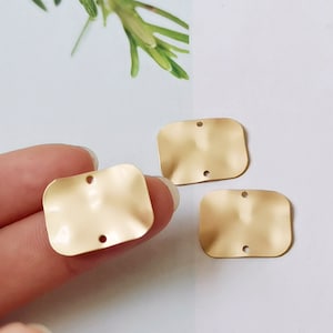 Pode incluir: Três pingentes retangulares de metal dourado com textura ondulada e dois furos cada.